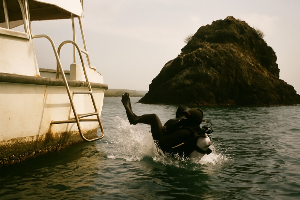 A diver entering the water from a boat ladder near a rocky islet