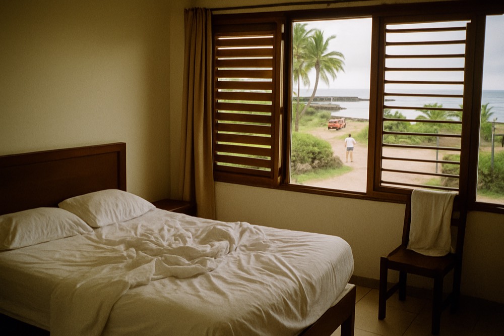 A bright hotel room with a double bed and open windows facing the sea