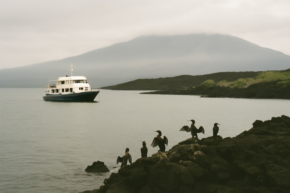 A small expedition yacht anchored in a calm bay between volcanic islands
